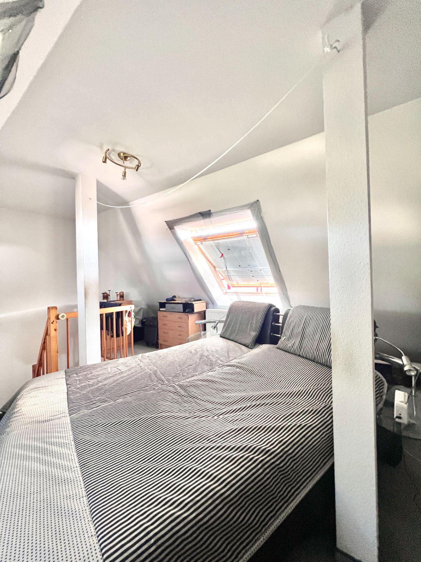 Dachzimmer mit Doppelbett, Schreibtisch unter Fenster und sichtbaren Holzbalken.