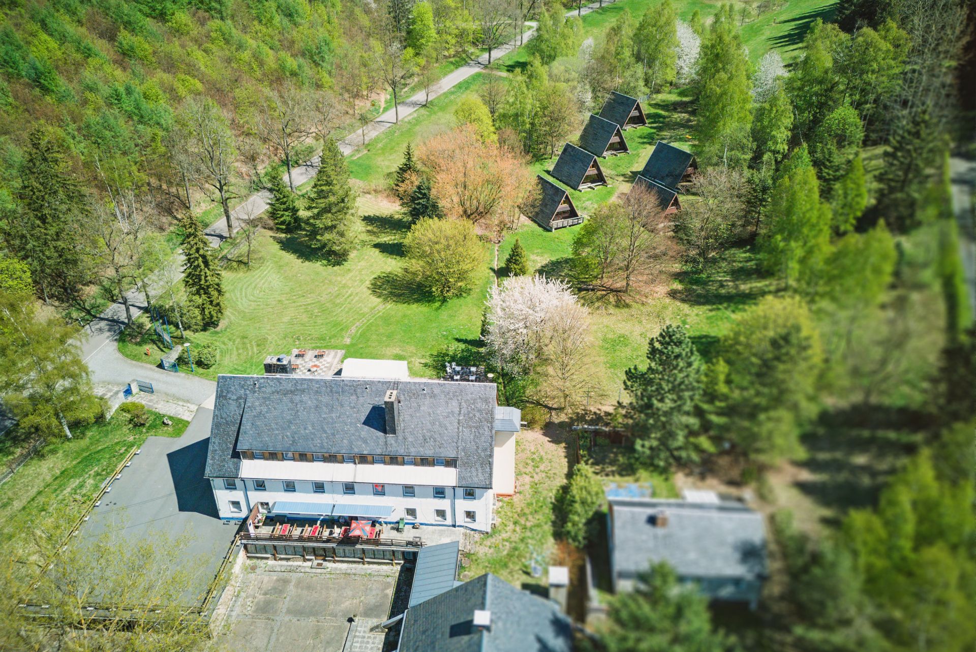Luftaufnahme eines Wohngebäudes mit Terrasse und mehreren Holzhäusern im grünen Garten.