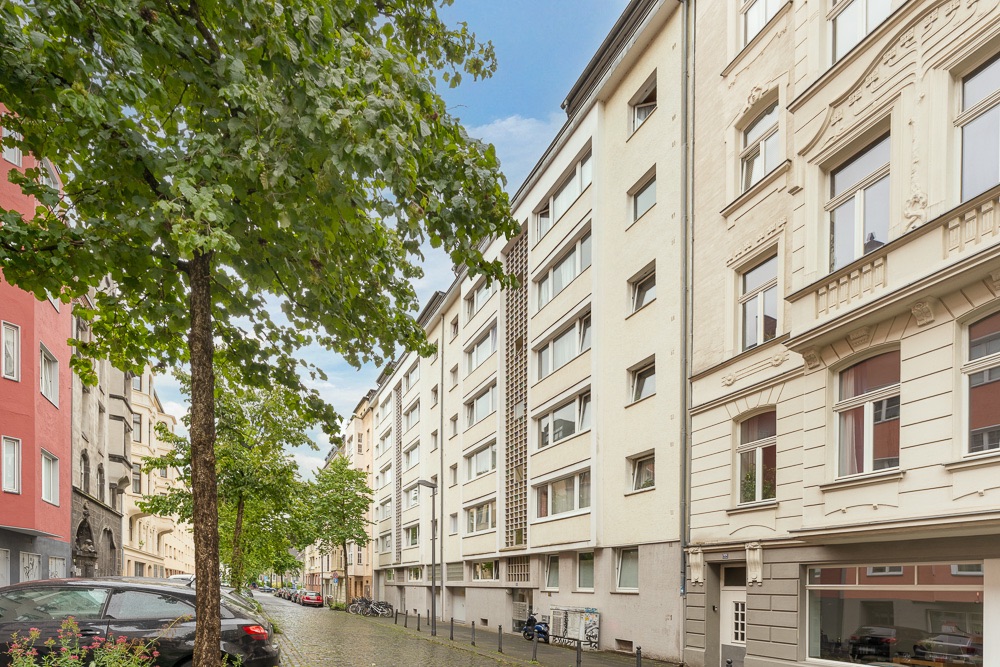 Wohnhäuser an einer ruhigen, baumbestandenen Straße mit parkenden Autos.