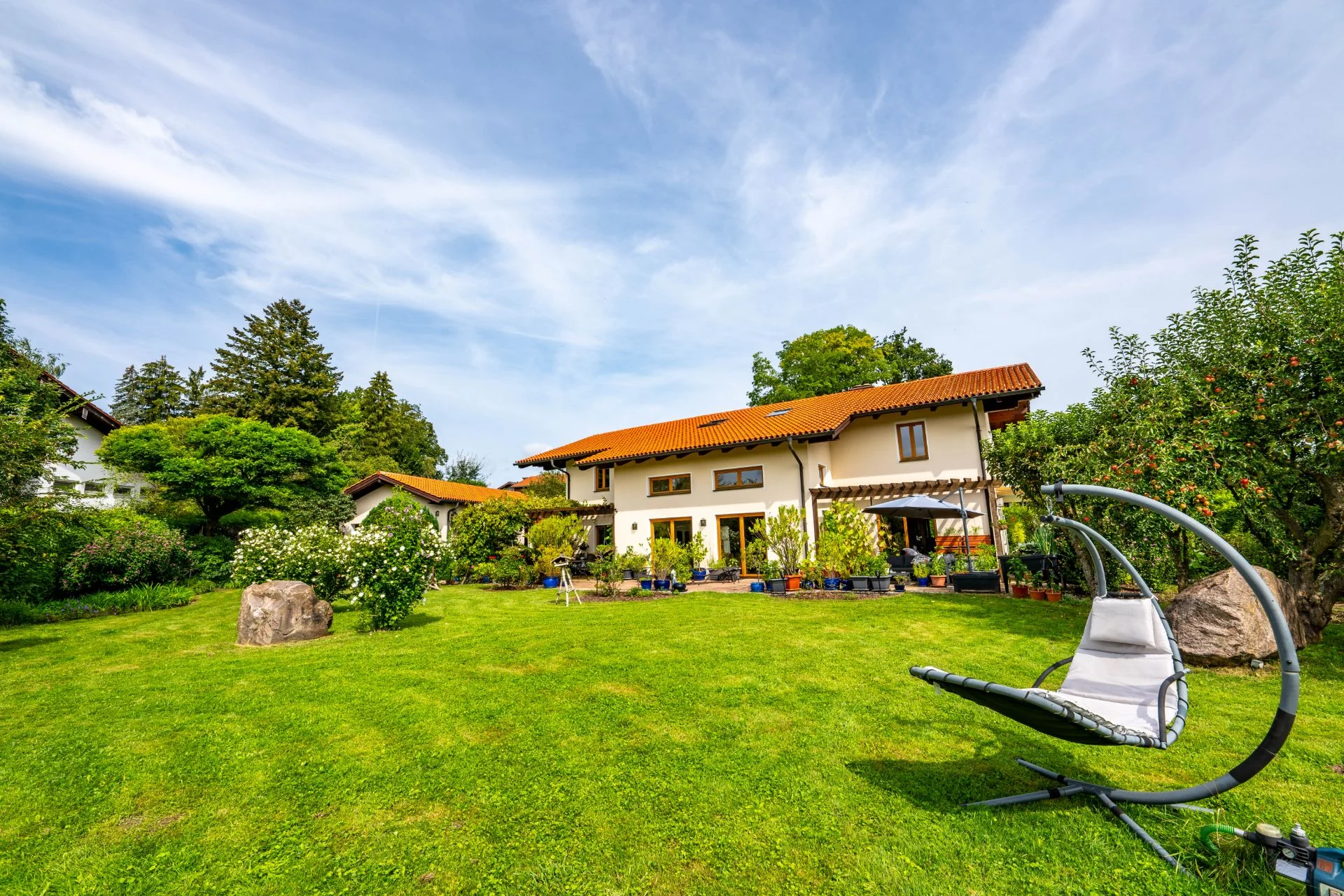 Zweistöckiges Haus mit rotem Dach, großem Garten und einer Hängeschaukel auf der Wiese.