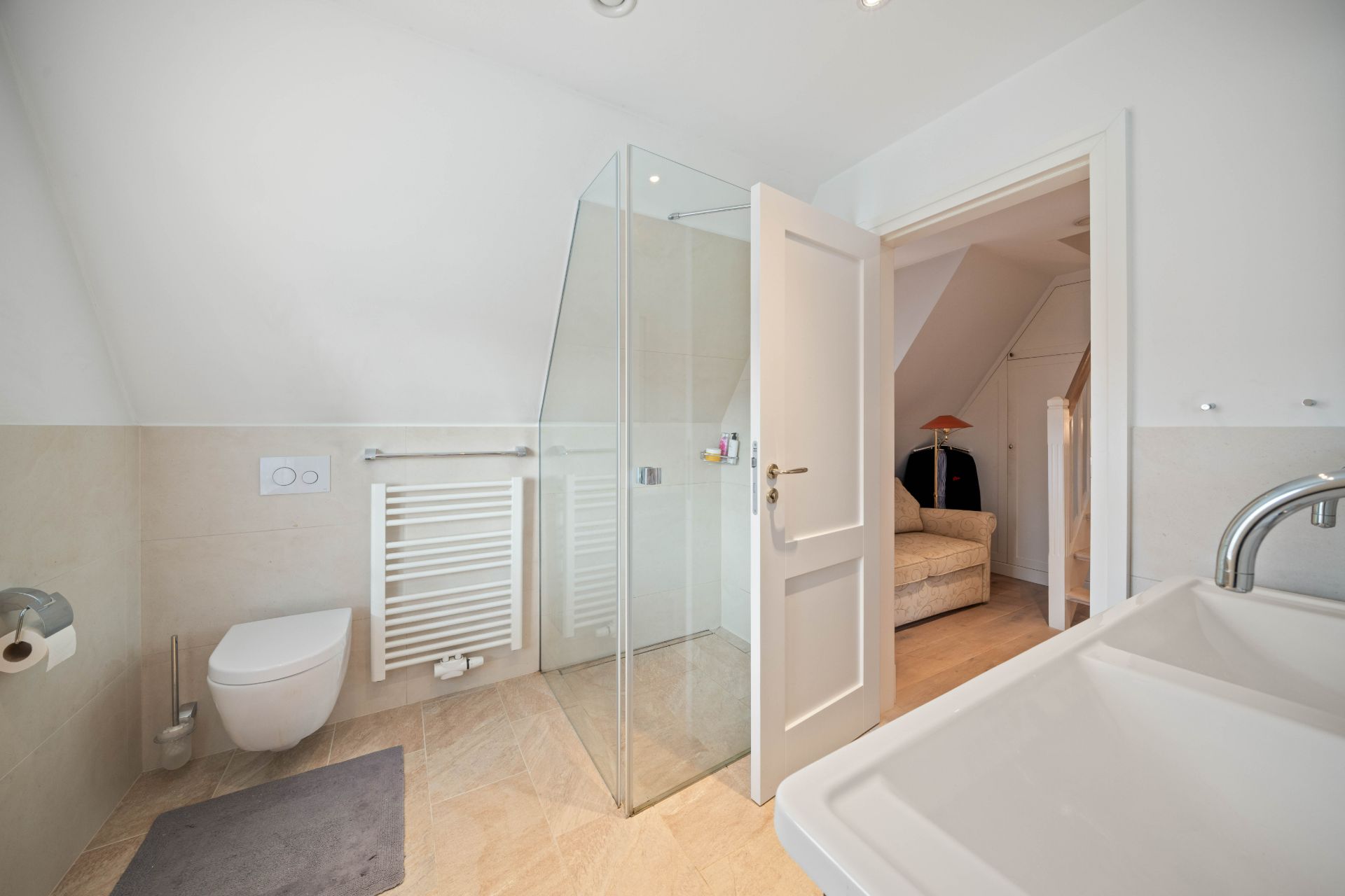 Modernes Badezimmer mit Dusche, WC, Waschbecken und offen stehender Tür zum angrenzenden Raum.