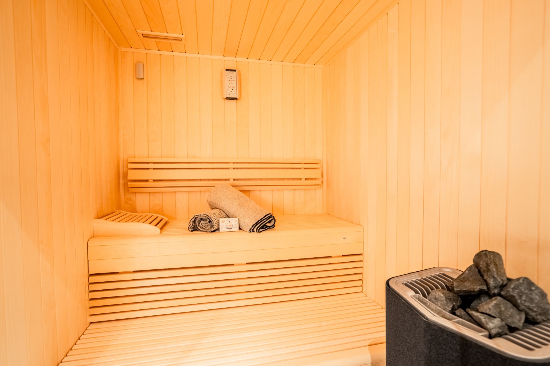 Helle Holzsauna mit Bank, Handtüchern und Saunaofen mit Steinen.