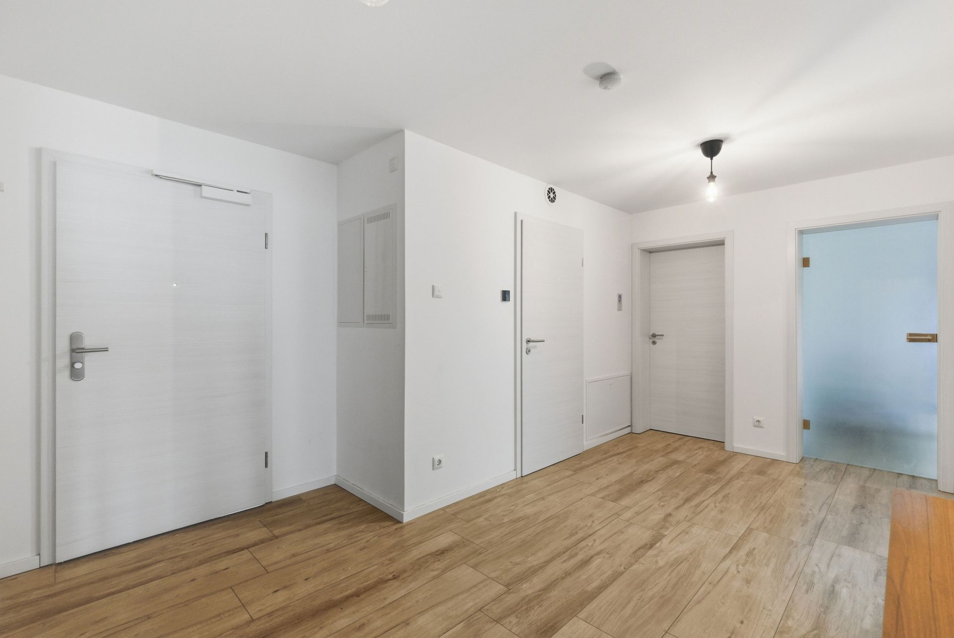 Heller Flur mit vier weißen Türen und Holzfußboden in einer Wohnung.