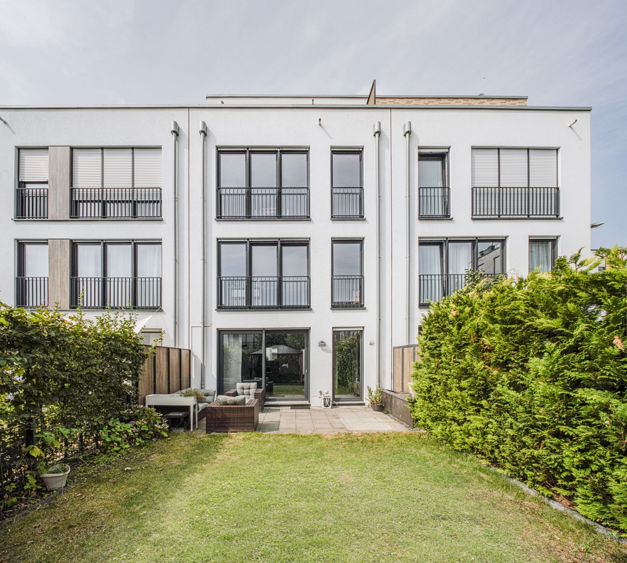 Moderne weiße Wohnhausfassade mit vielen Fenstern und kleinem Garten im Vordergrund.