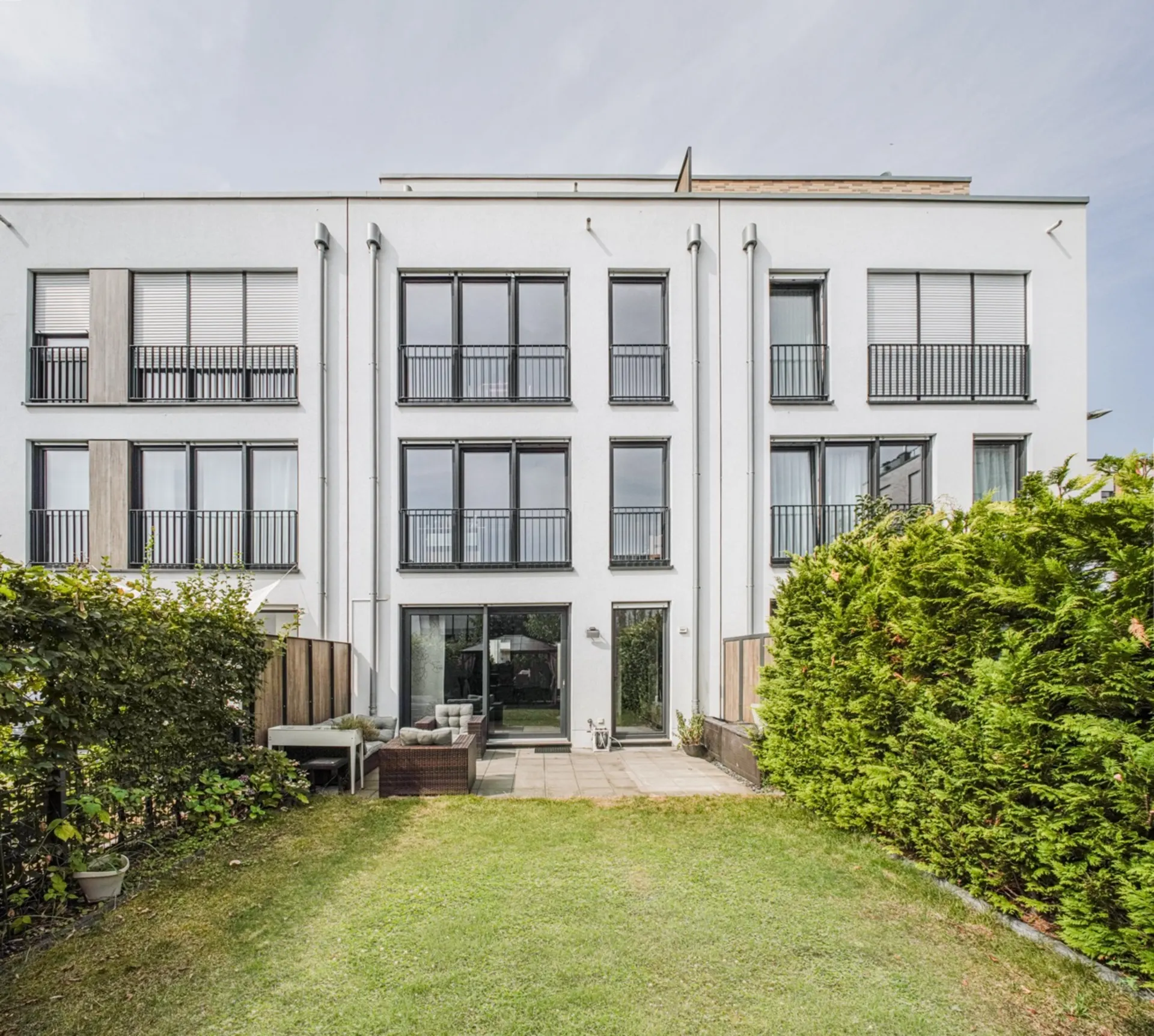 Moderne weiße Wohnhausfassade mit vielen Fenstern und kleinem Garten im Vordergrund.