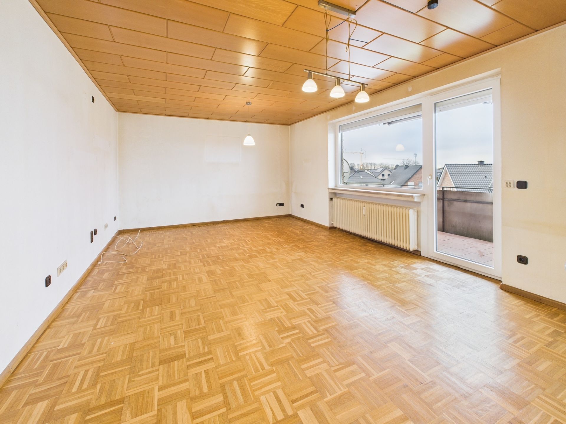 Leerer Raum mit Parkettboden, Holzdecke, großen Fenstern und Zugang zum Balkon.