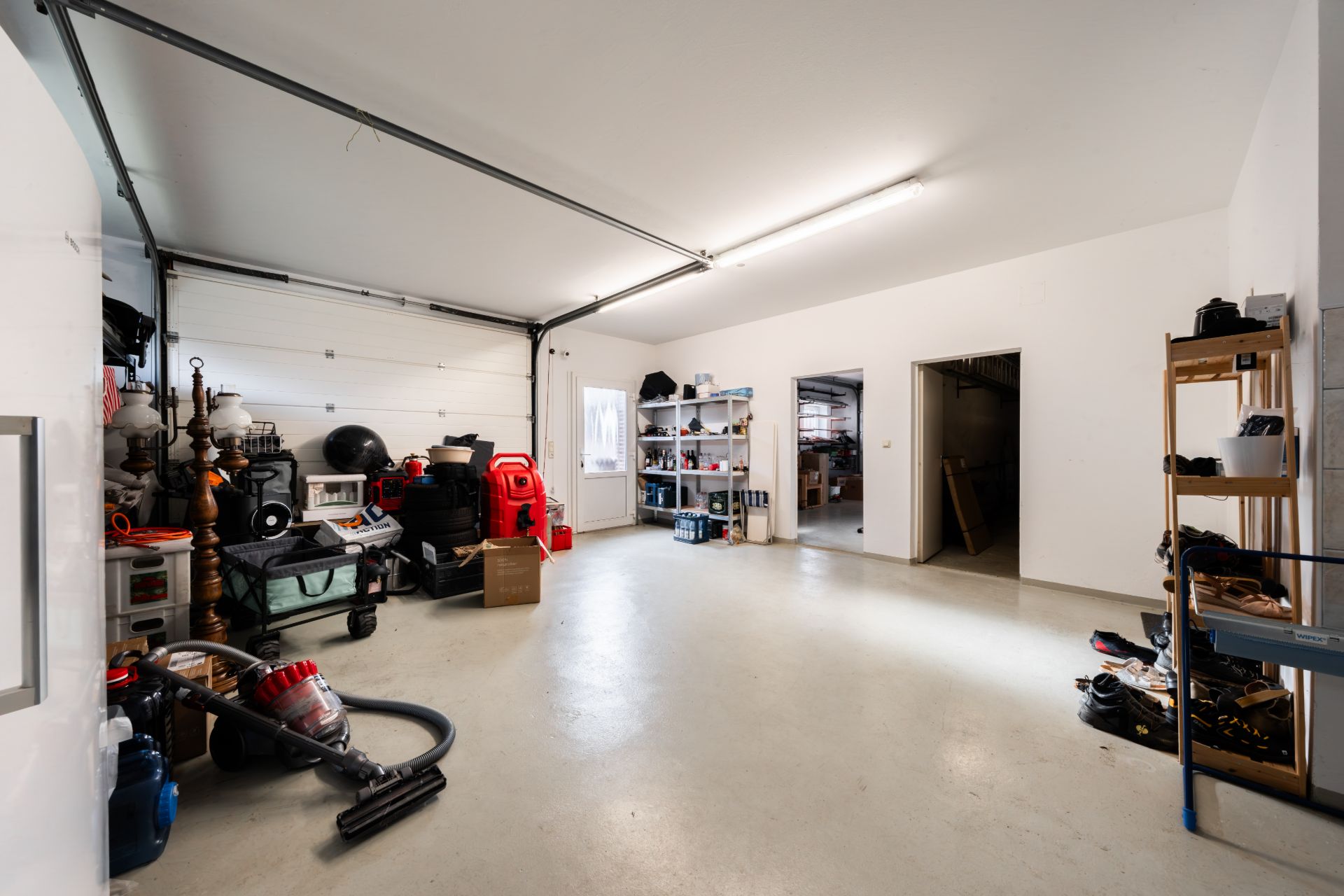 Geräumige Garage mit Regalen, Werkzeugen und Haushaltsgegenständen an den Wänden.