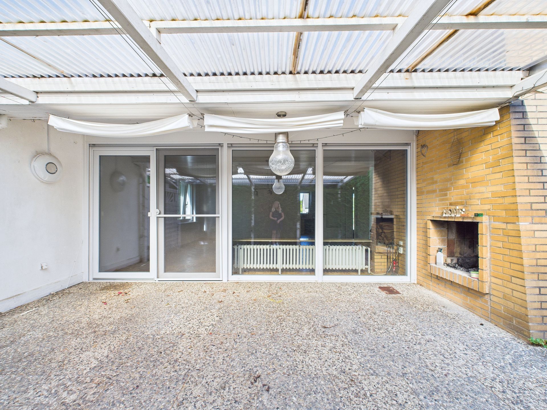 Überdachte Terrasse mit Glas-Schiebetüren und gemauertem Kamin an einer Hauswand.