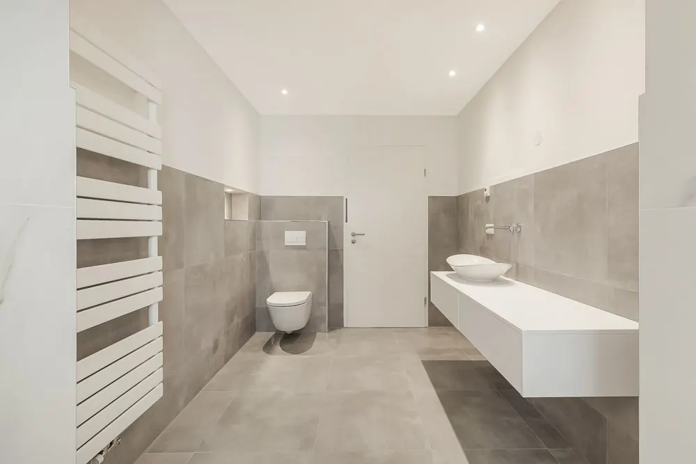 Modernes Badezimmer mit wandhängender Toilette, Waschbecken und grauen Fliesen.