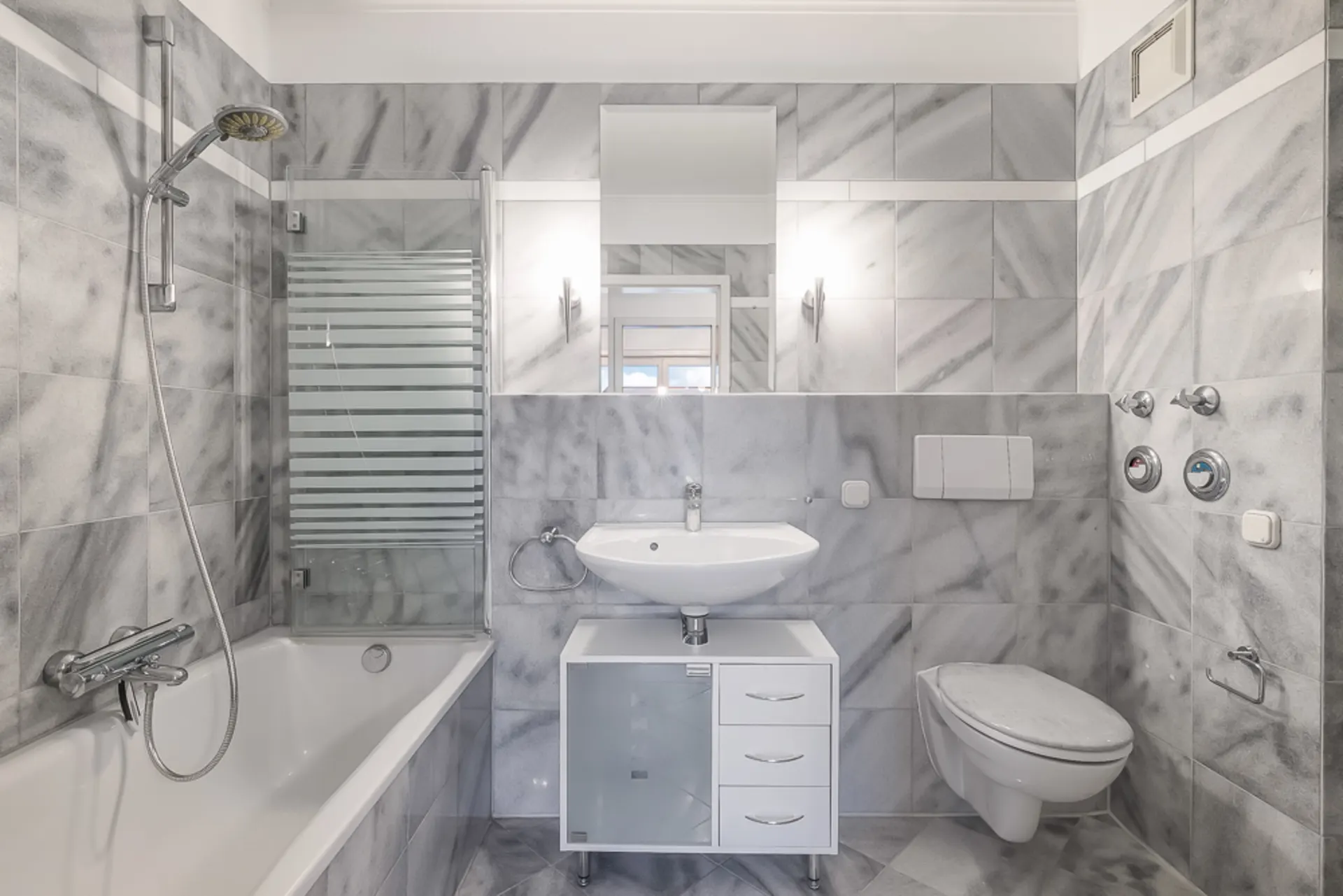 Modernes Badezimmer mit Badewanne, Dusche, Waschbecken, Spiegel und Wand-WC, alles in grauen Fliesen.