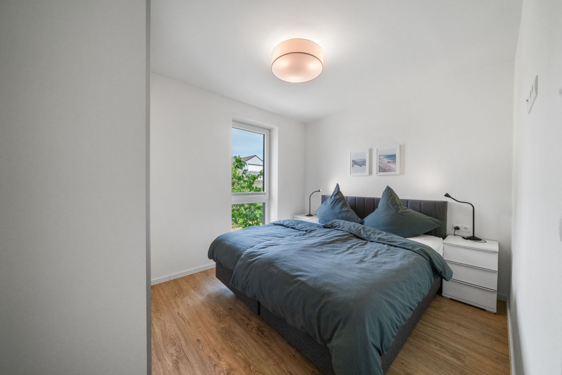 Helles Schlafzimmer mit Doppelbett, zwei Nachttischen, Fenstern und Holzfußboden.
