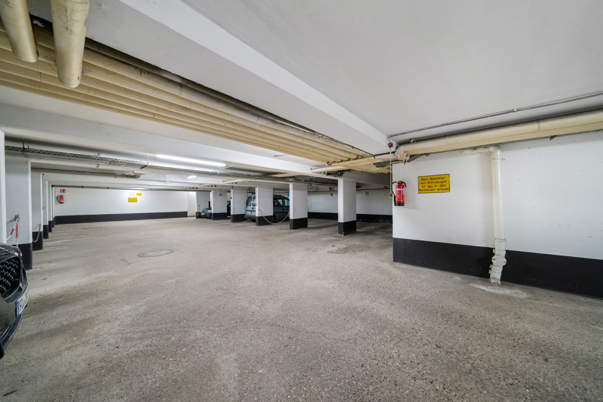 Leere Tiefgarage mit sichtbaren Rohren und weißen Wänden.