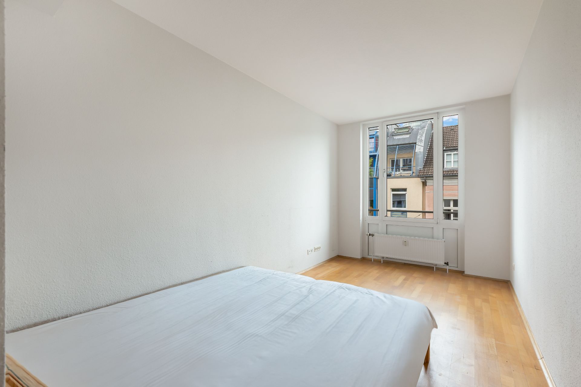Helles Schlafzimmer mit Holzboden, einem Bett und großem Fenster mit Blick nach draußen.