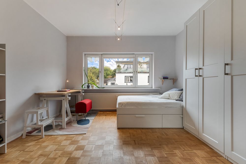 Helles Schlafzimmer mit Bett, großem Kleiderschrank, Schreibtisch und Fenster mit Ausblick.