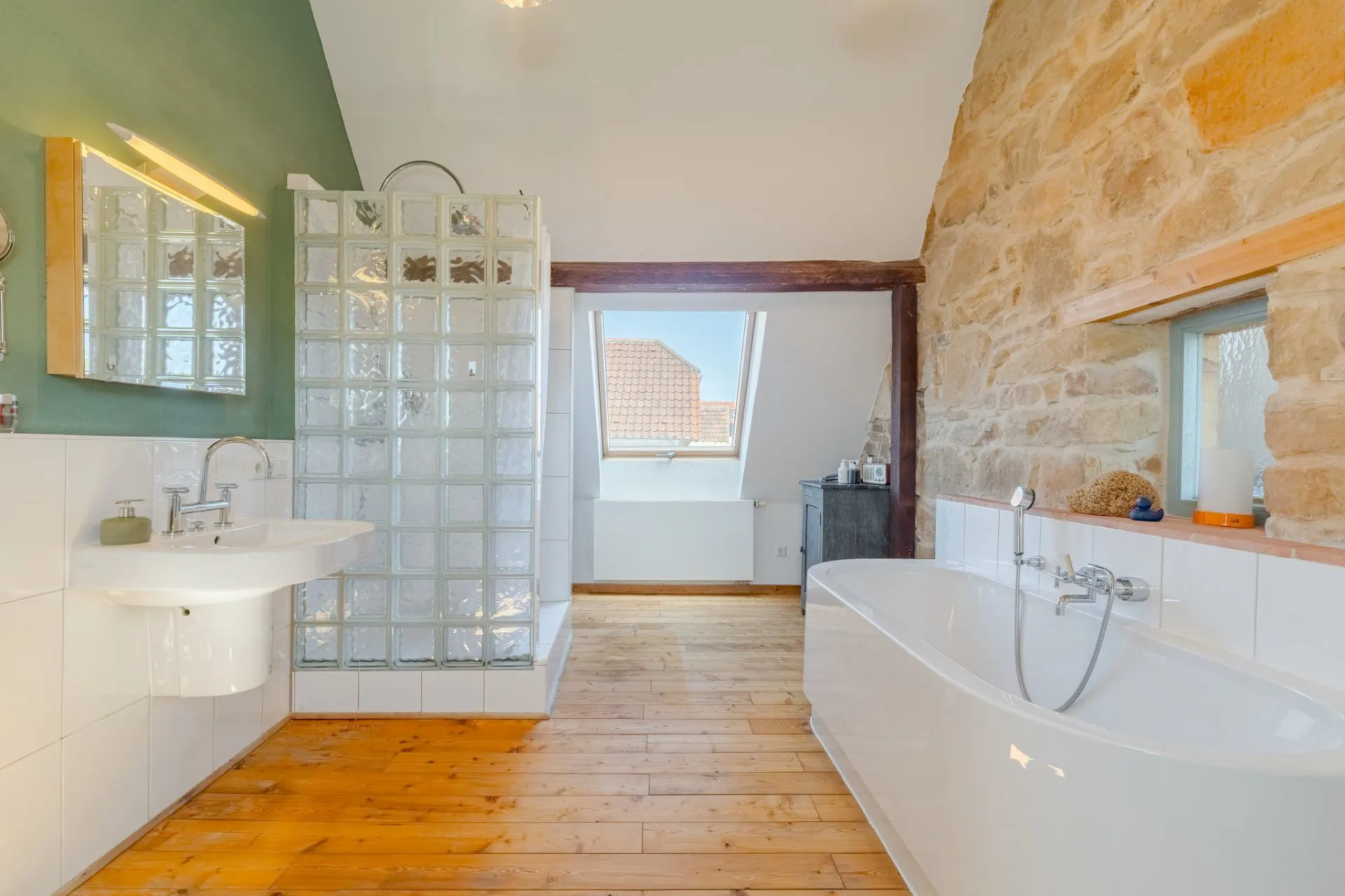 Helles Badezimmer mit Dusche aus Glasbausteinen, freistehender Badewanne und Holzboden.