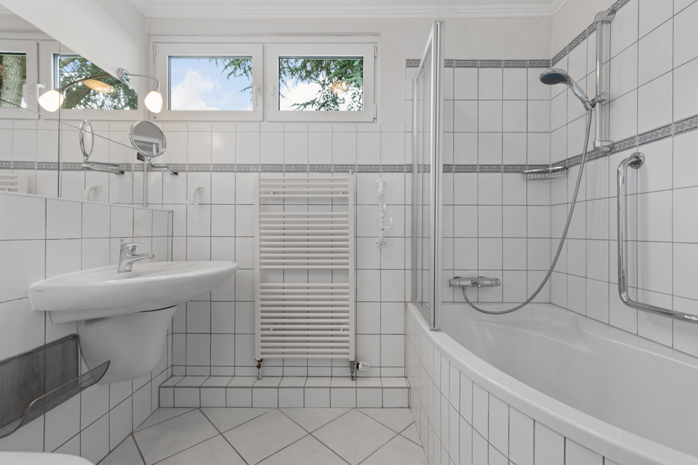 Helles Badezimmer mit Badewanne, Dusche, Waschbecken und Handtuchheizkörper.