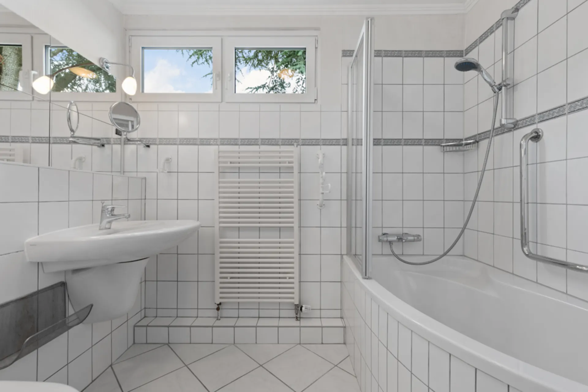 Helles Badezimmer mit Badewanne, Dusche, Waschbecken und Handtuchheizkörper.