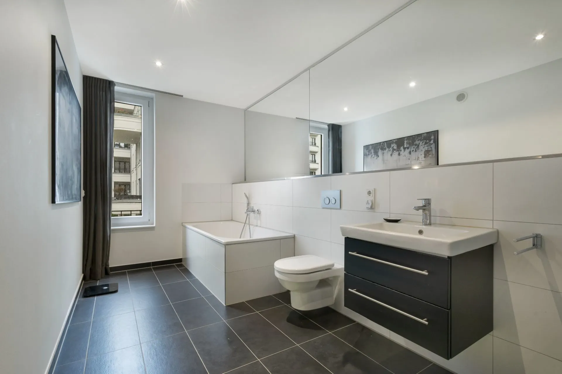 Modernes Badezimmer mit Badewanne, Hänge-WC, Waschtisch und großem Spiegel.