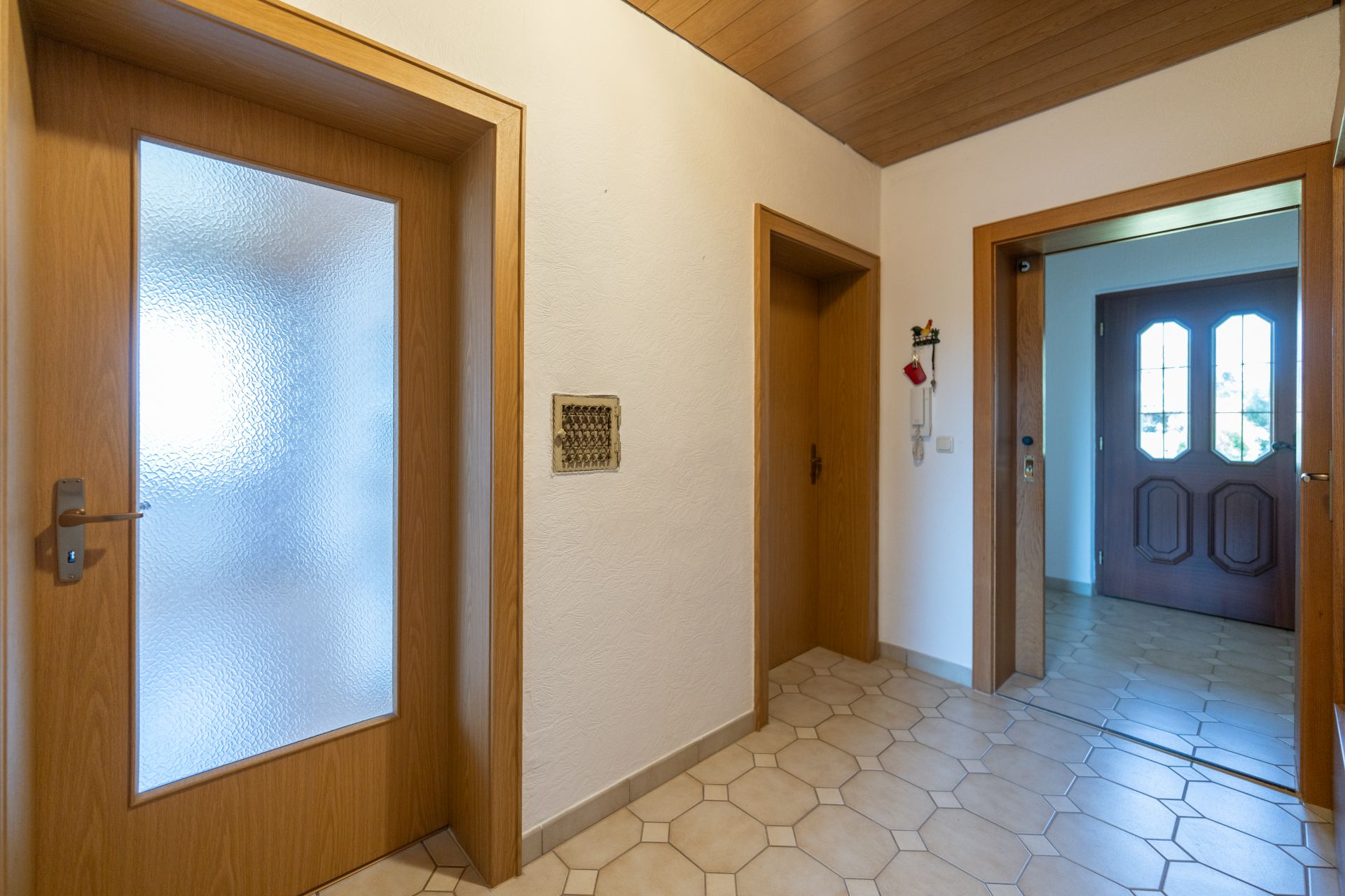 Heller Flur mit Holztüren, Fliesenboden und Blick auf einen Eingang mit Glastür.