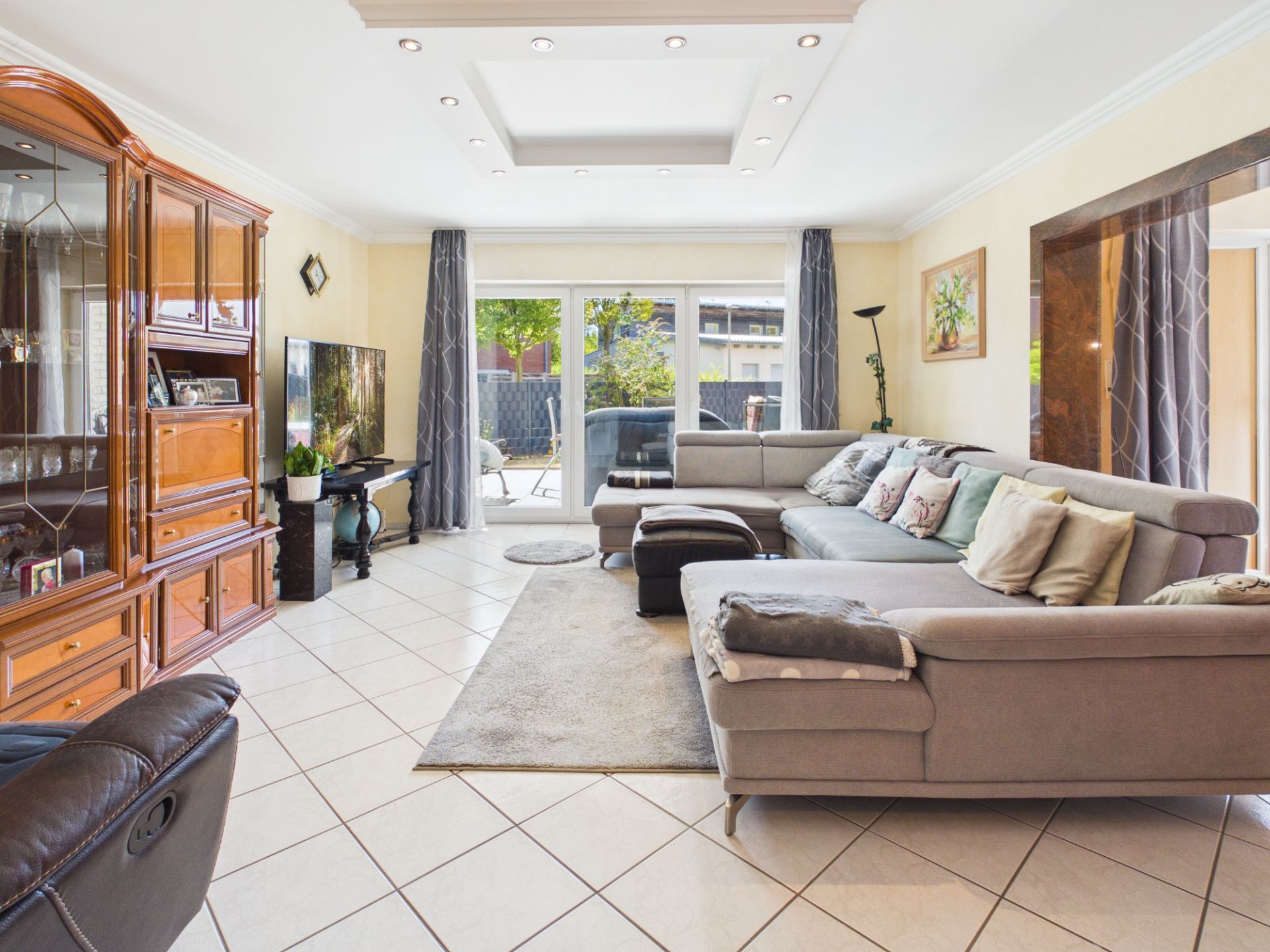 Helles Wohnzimmer mit großer Eckcouch, Wohnwand, Fernseher und Zugang zur Terrasse.