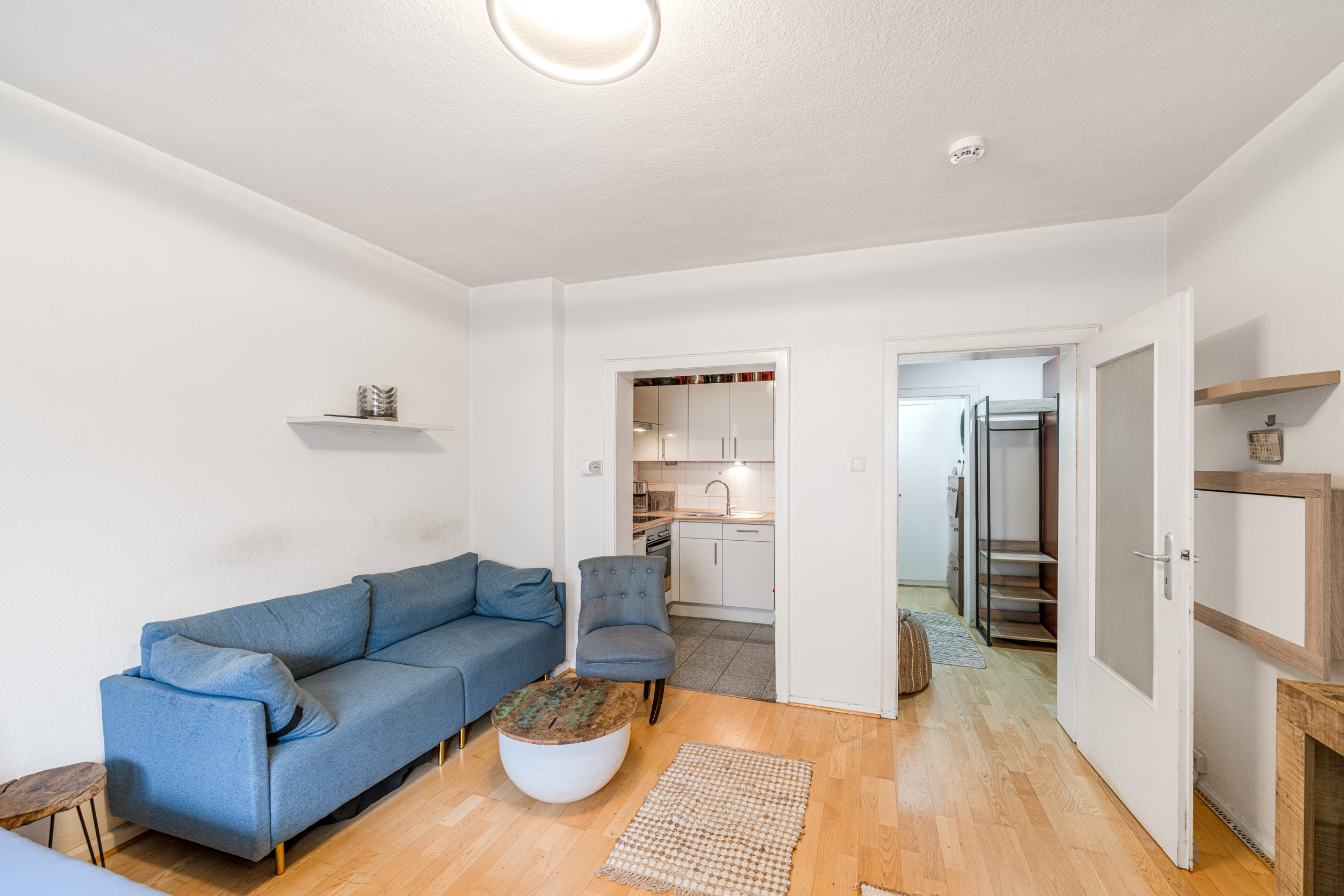 Wohnzimmer mit blauem Sofa, Sessel, Couchtisch und Blick in Küche sowie Flur.