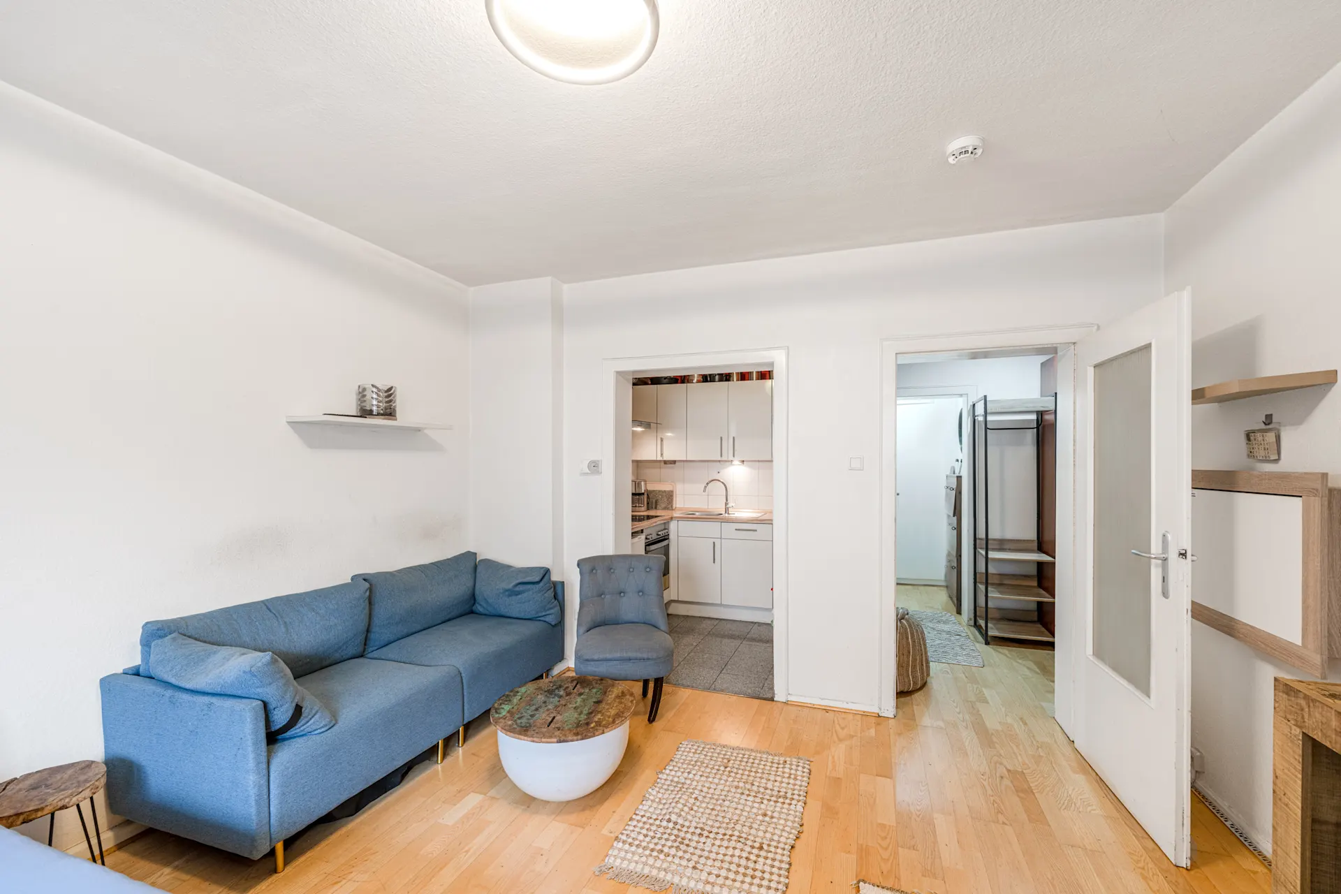 Wohnzimmer mit blauem Sofa, Sessel, Couchtisch und Blick in Küche sowie Flur.
