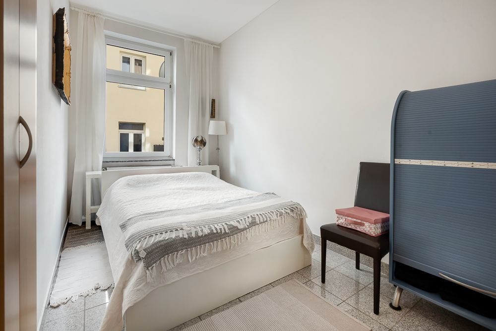 Kleines Schlafzimmer mit Bett, Stuhl, Fenster und blauem Schrank.