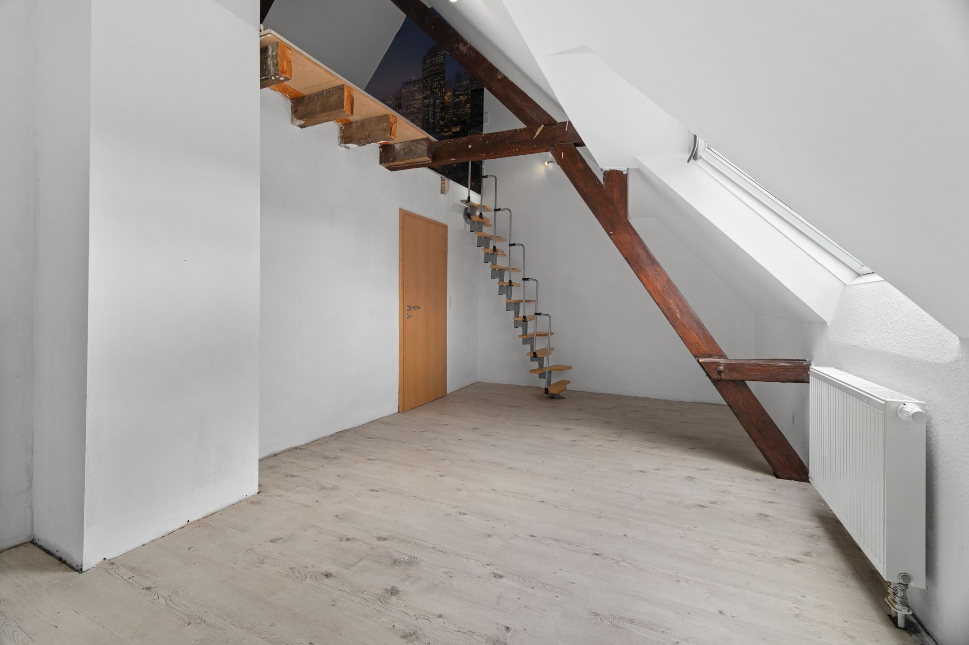 Helles Dachzimmer mit Holztreppe zu einer Galerie und großem Fenster.