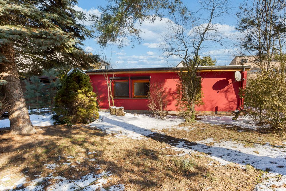 Rotes einstöckiges Haus mit Flachdach, Bäumen und etwas Schnee im Garten.