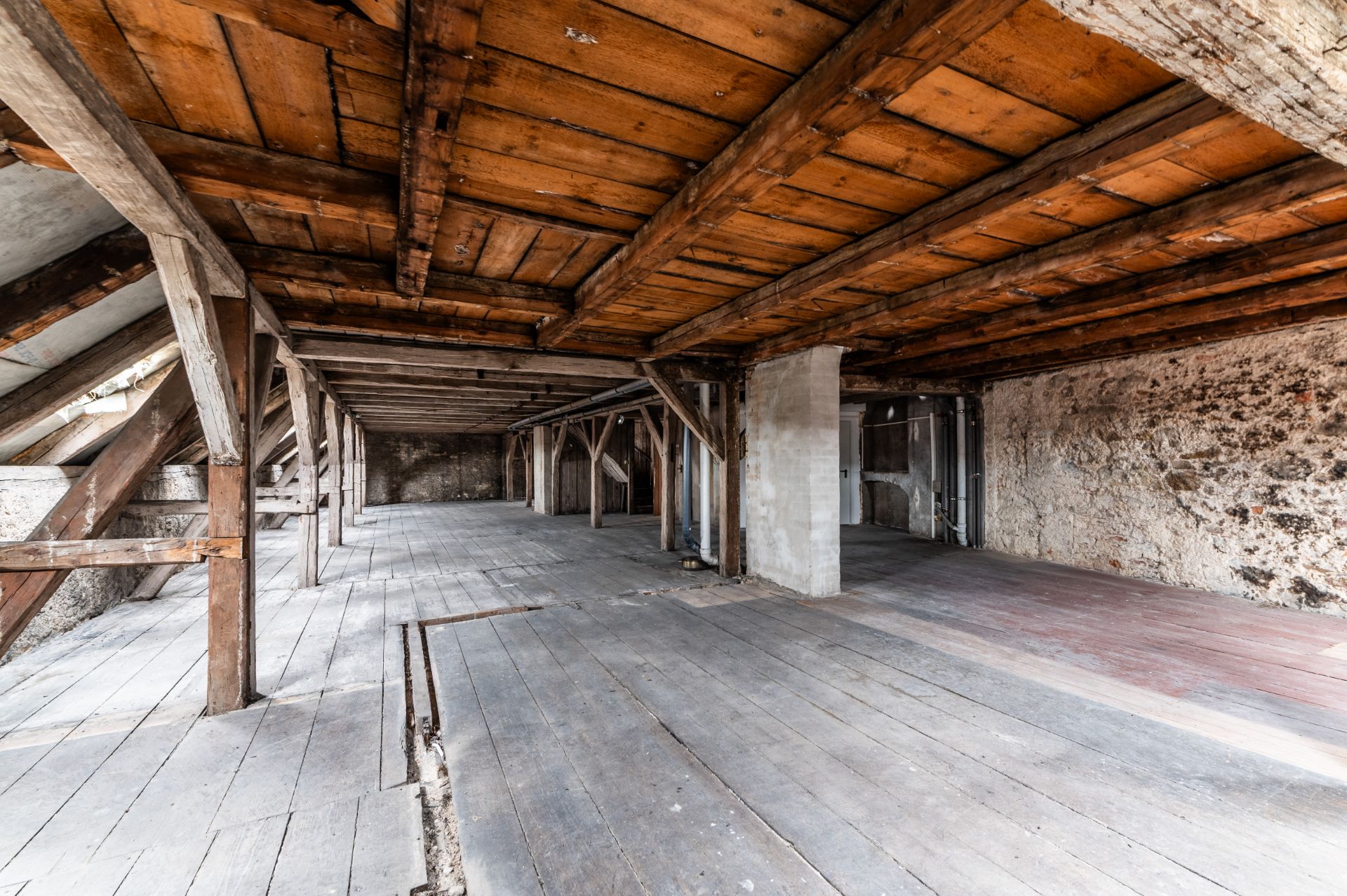Großer, leerer Dachboden mit Holzbalken, Holzdecke und unverputzten Steinwänden.