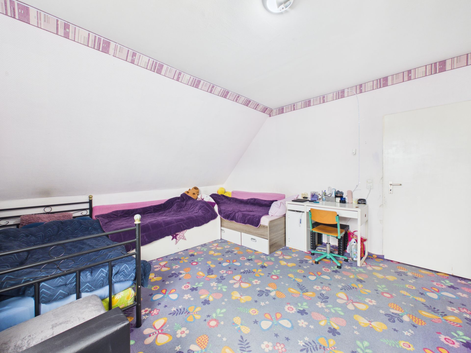 Kinderzimmer mit zwei Betten, Schreibtisch und buntem Teppich mit Schmetterlingsmuster.