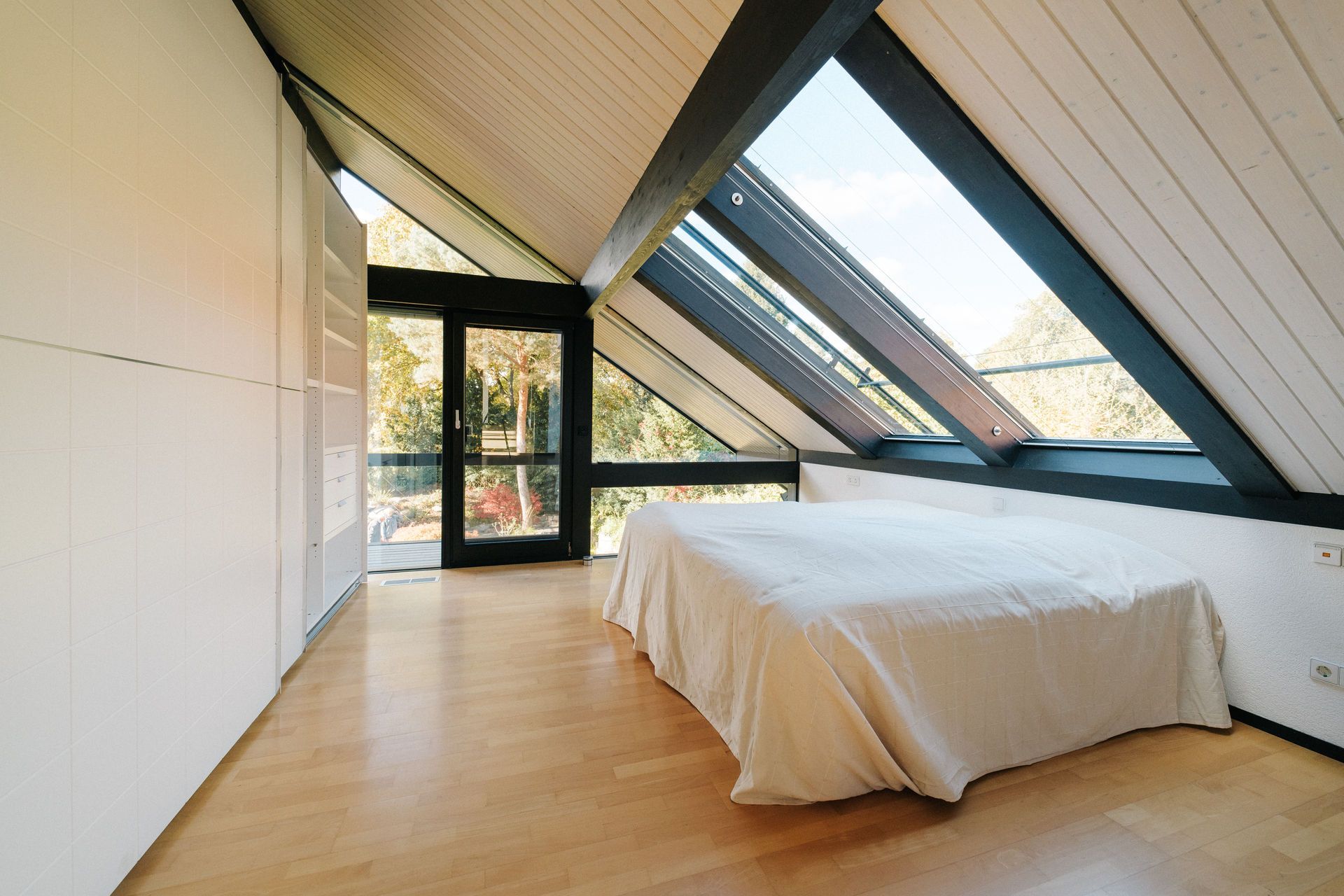 Schlafzimmer mit Dachschräge, großem Fenster und Bett auf hellem Holzboden.