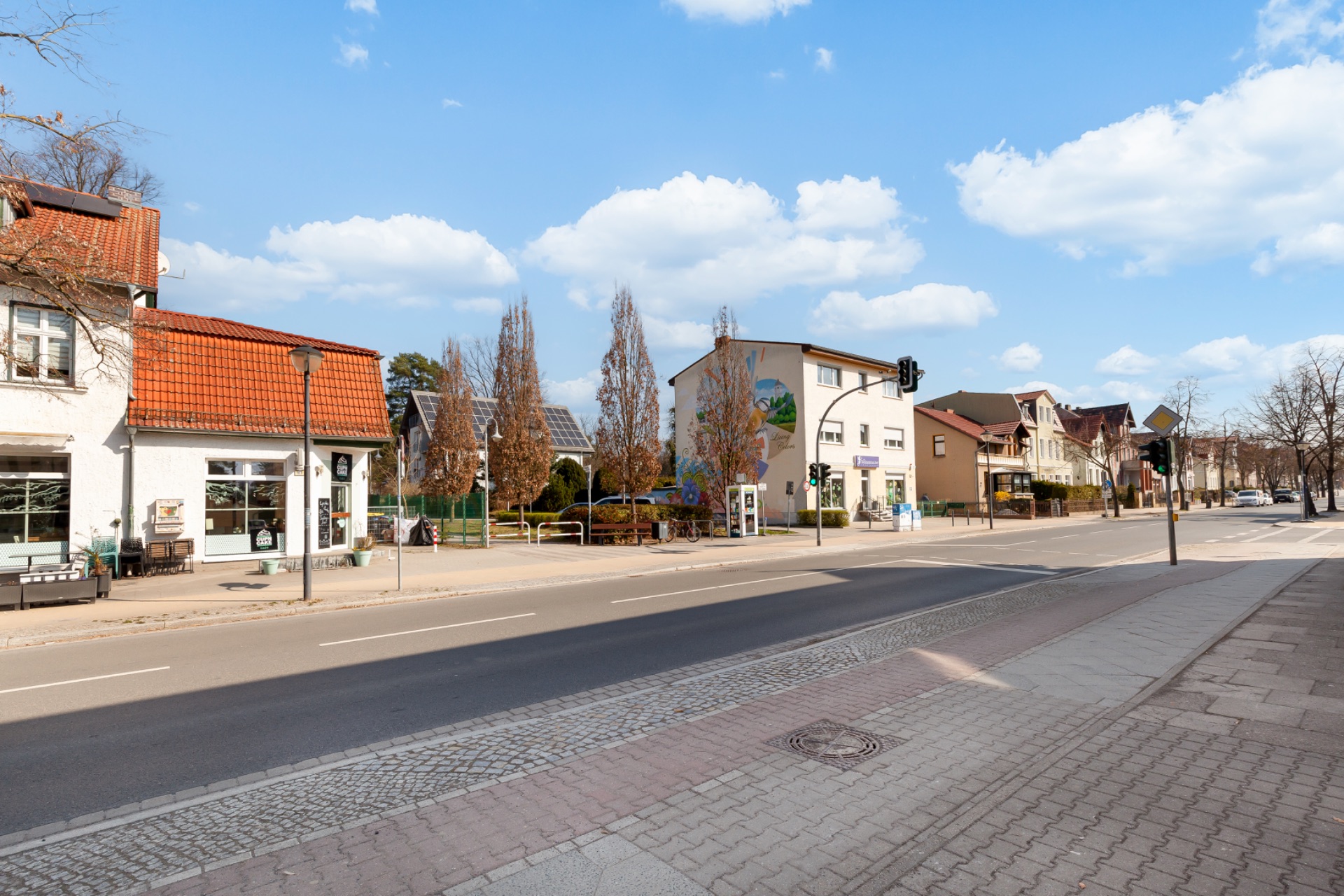 Straßenszene mit Gehweg, Wohnhäusern und Bäumen an einem sonnigen Tag.