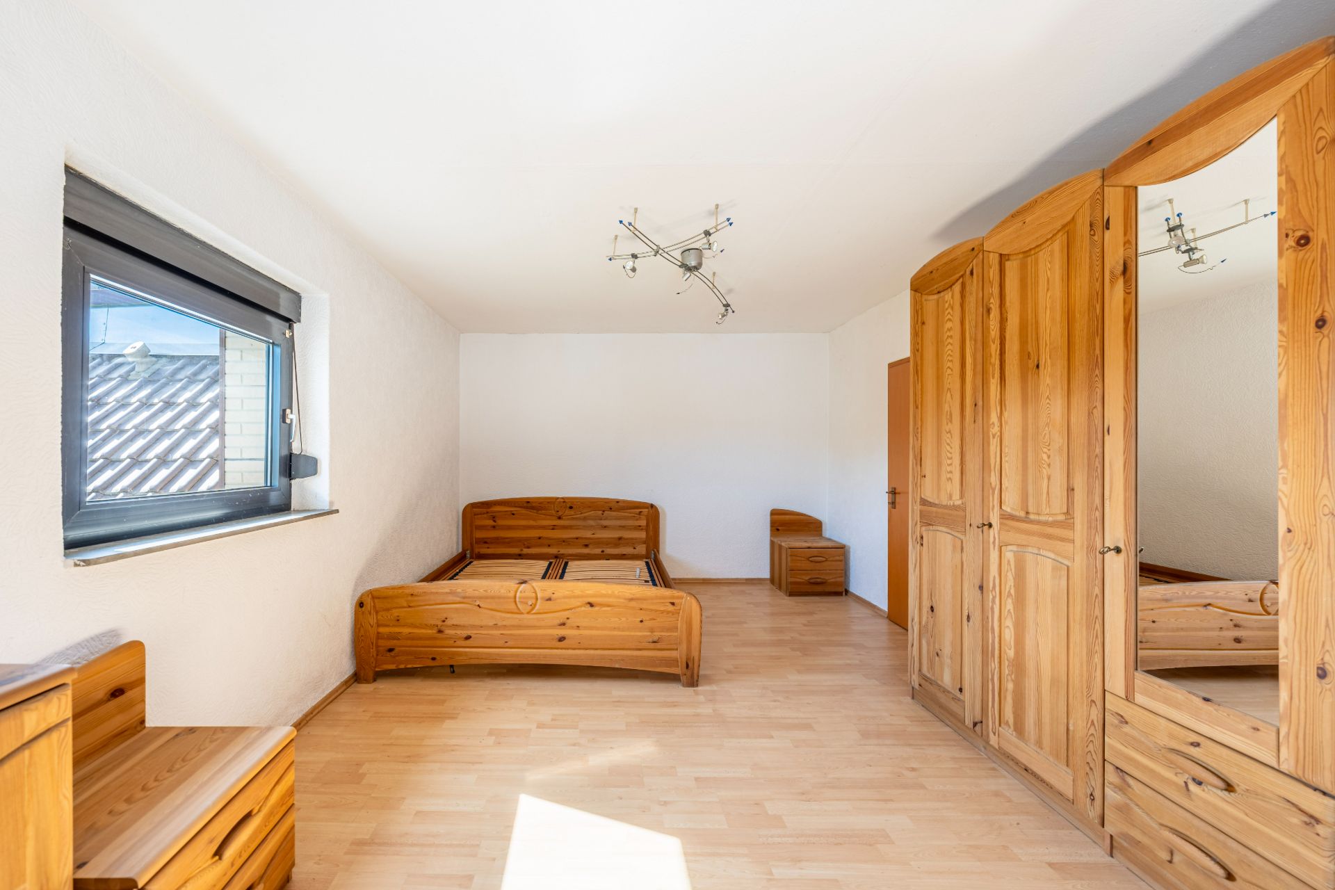 Helles Schlafzimmer mit Holzbett, Kleiderschrank mit Spiegel und Fenster.