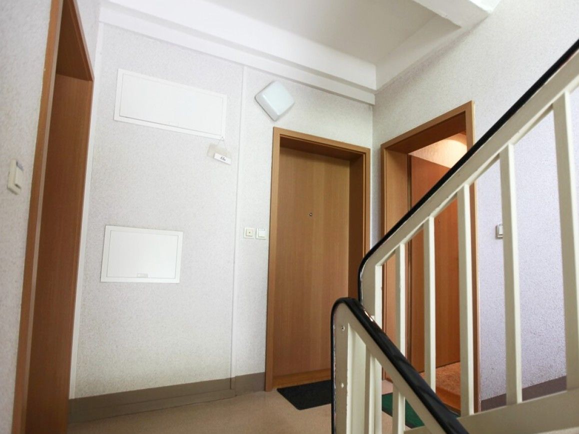 Treppenhaus mit zwei Holztüren und einem weißen Geländer.