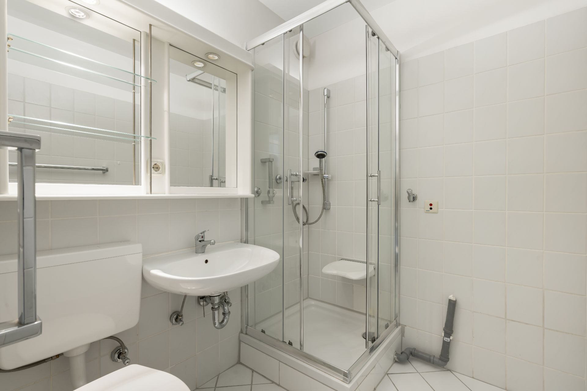 Modernes, weiß gefliestes Badezimmer mit Dusche, Waschbecken, Spiegel und Toilette.