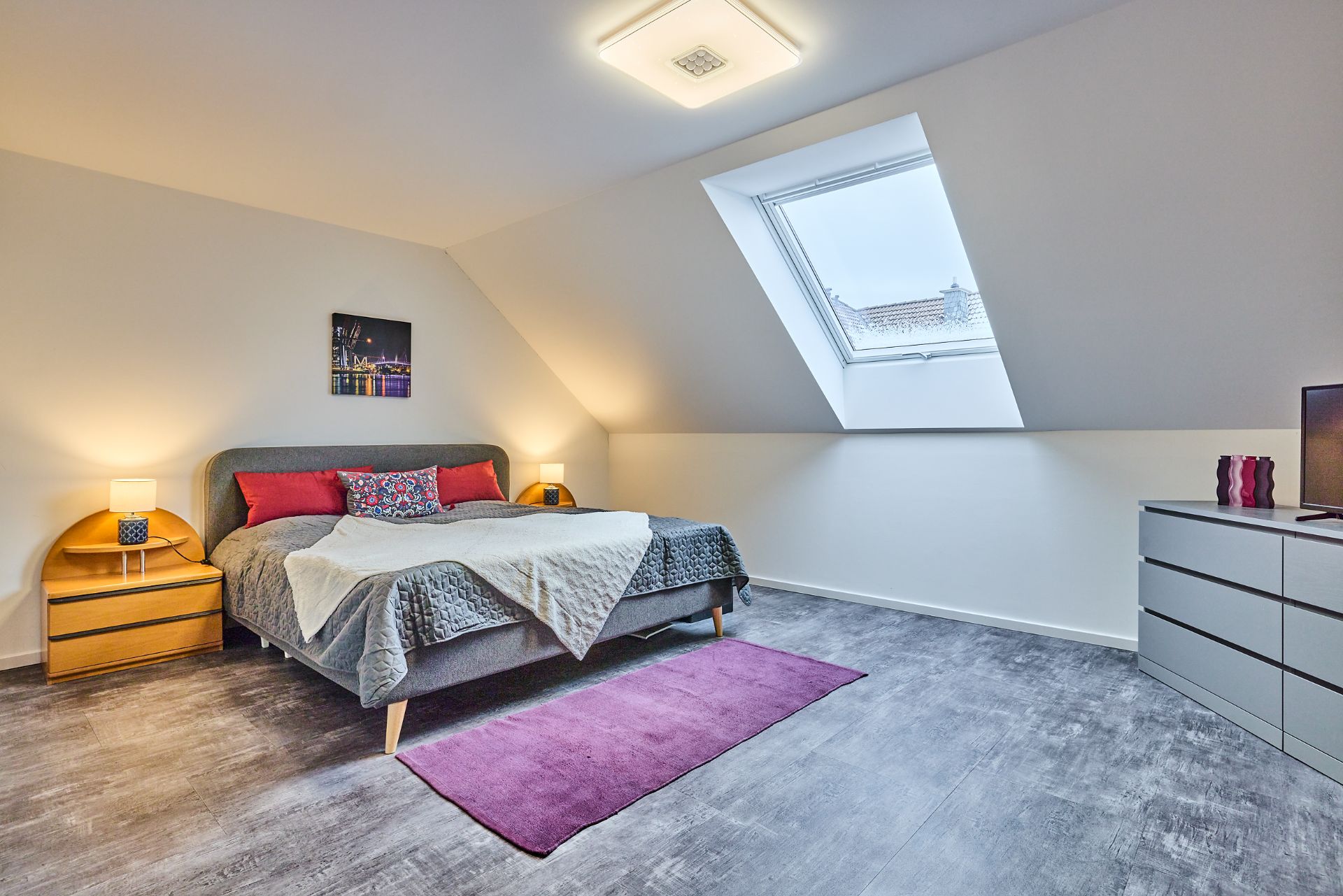 Modernes Schlafzimmer mit Doppelbett, Dachfenster und zwei Nachttischen mit Lampen.