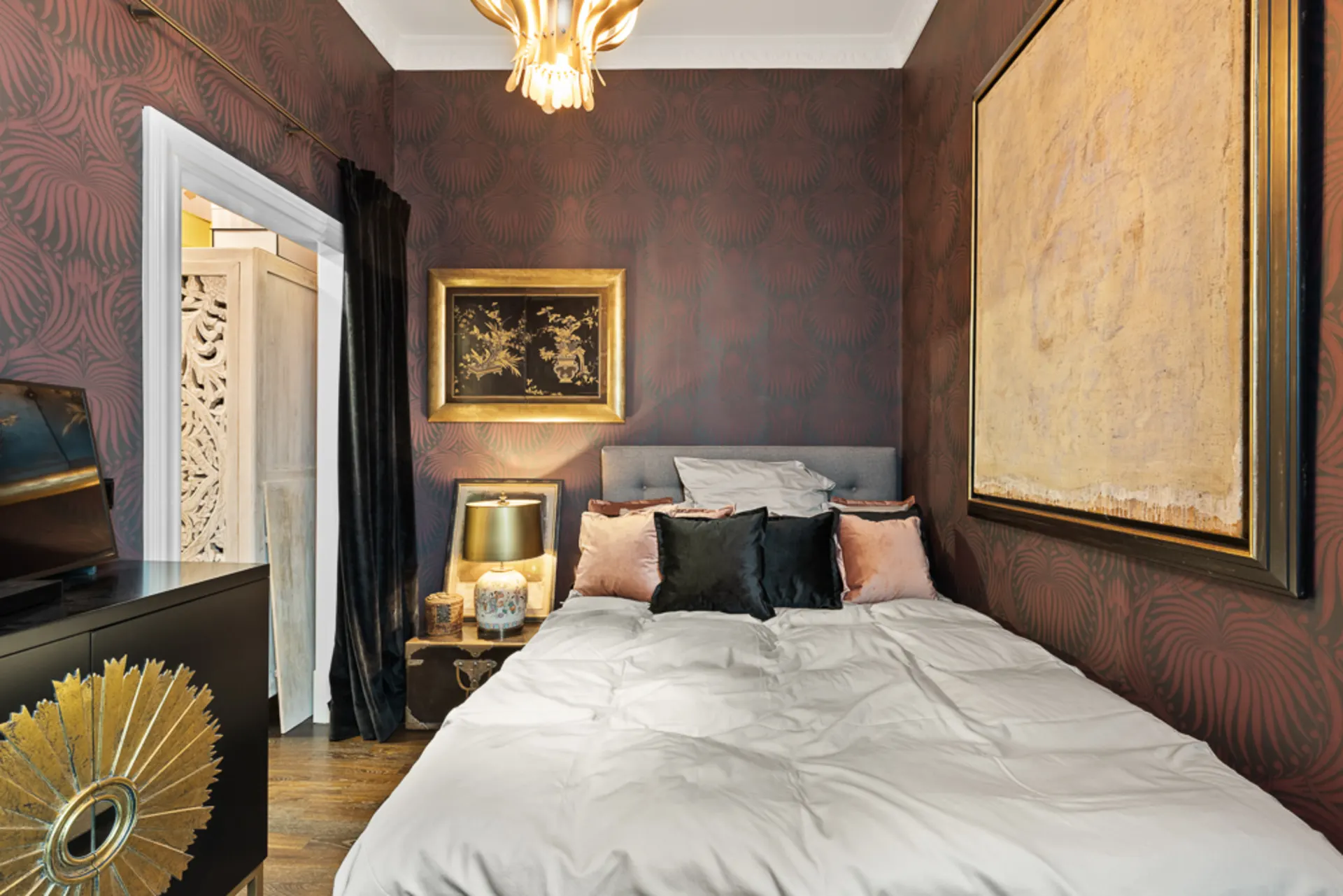 Kleines Schlafzimmer mit Doppelbett, dekorativen Kissen, Wandkunst und dunkler Tapete.