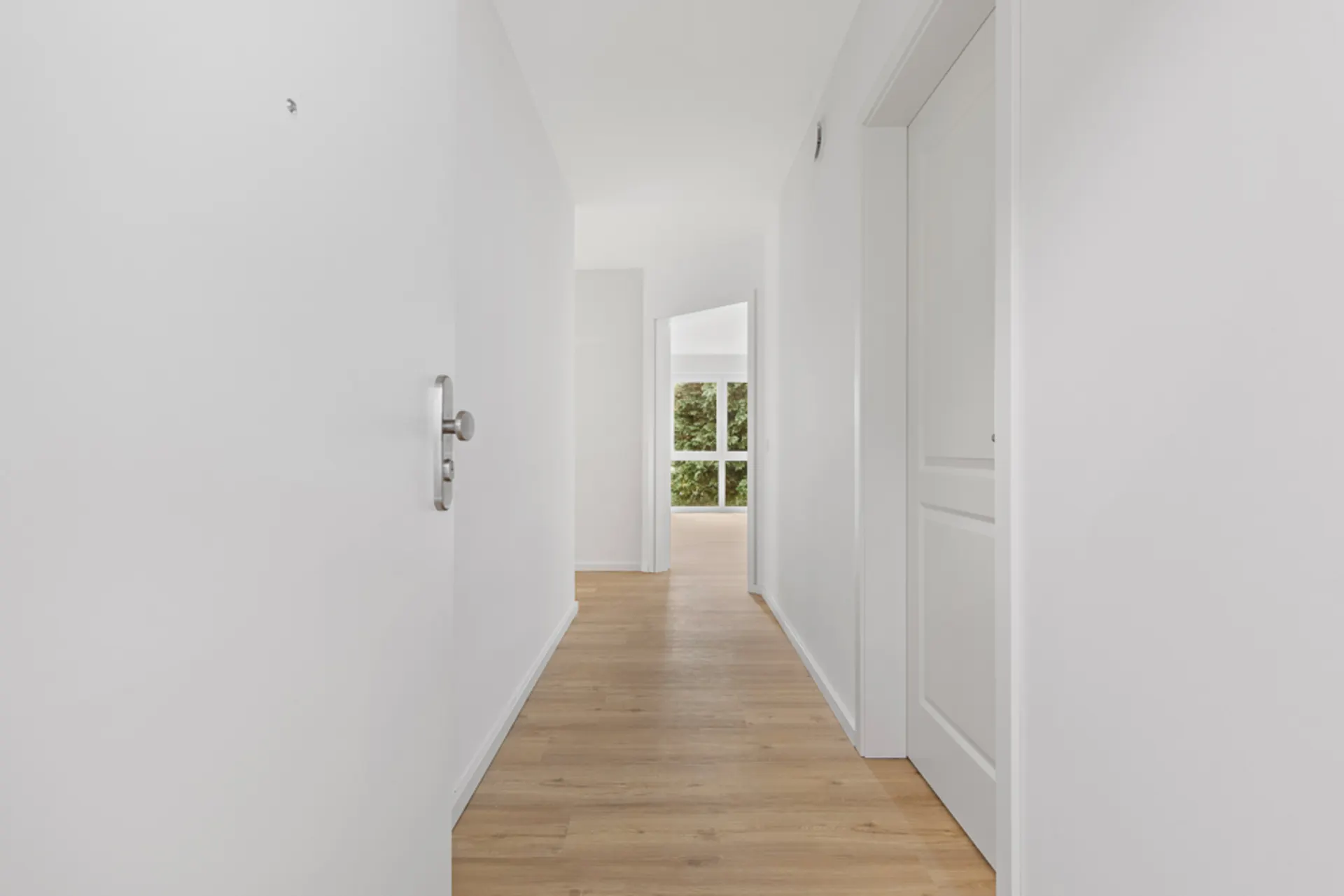 Heller Flur mit Holzboden, weißen Wänden und Türen, großes Fenster am Ende.