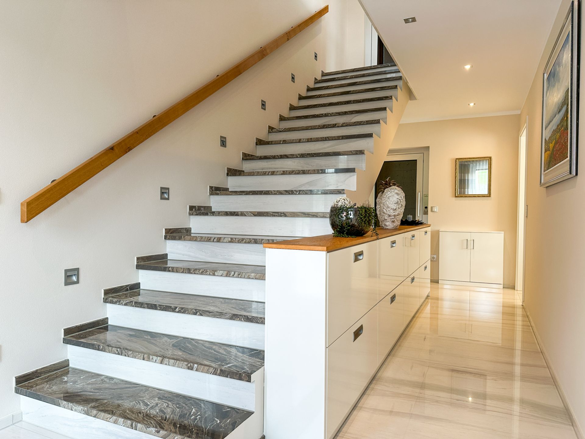 Moderne Treppe mit Marmorstufen und weißen Schubladen im Flur eines Wohnhauses.