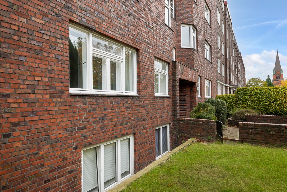 Backsteinwohnhaus mit mehreren Fenstern und kleinem Garten davor.