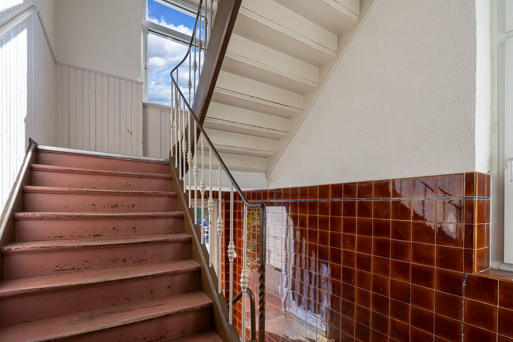 Treppe mit roten Stufen, braunen Fliesen an der Wand und Fenster mit Blick nach draußen.