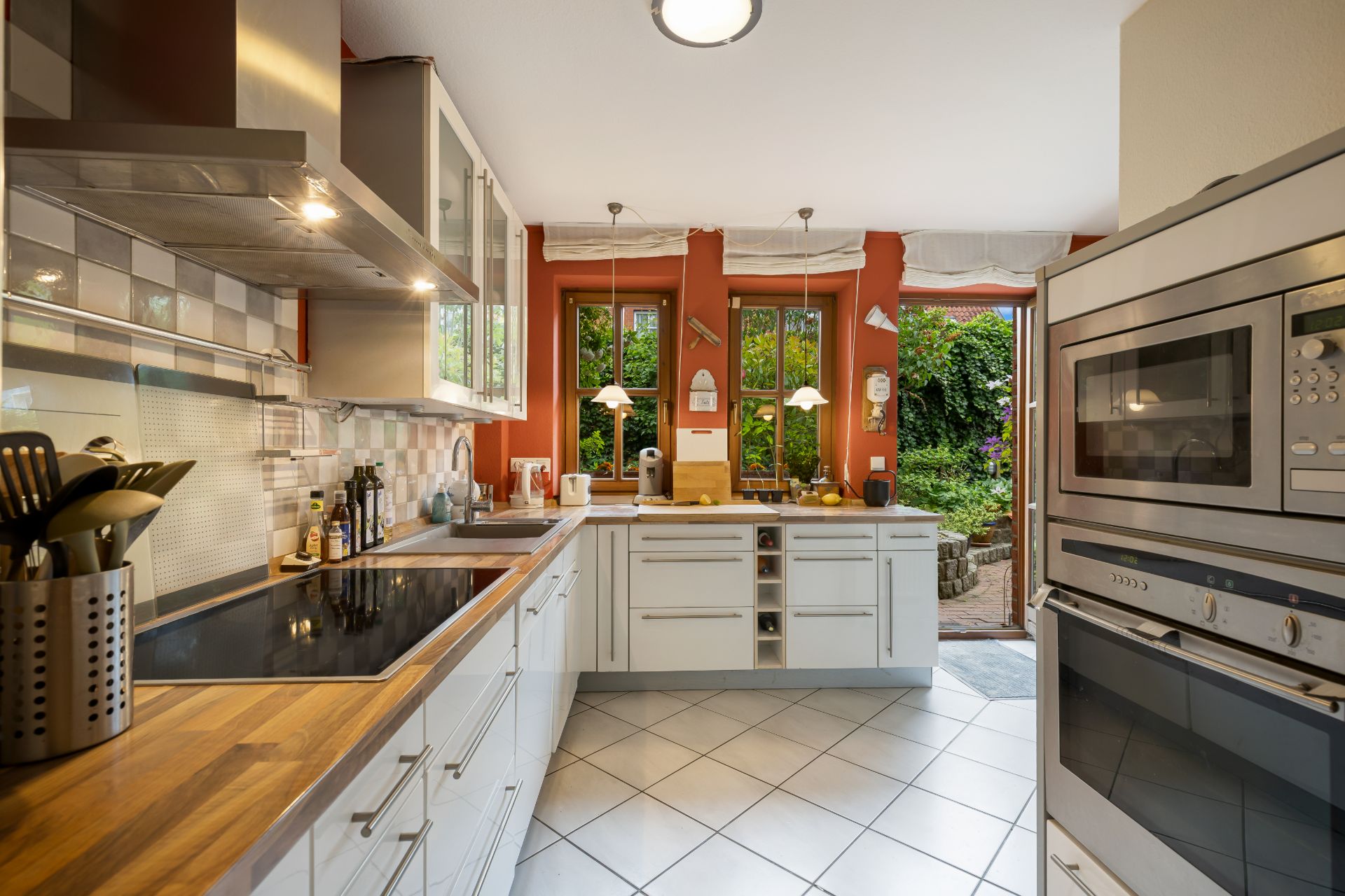 Helle Küche mit weißen Schränken, Herd, Backofen und Blick in einen grünen Garten.