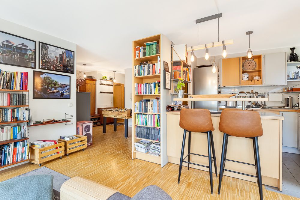 Helles Wohnzimmer mit Bücherregalen, offener Küche, Barhockern und einem Kickertisch.