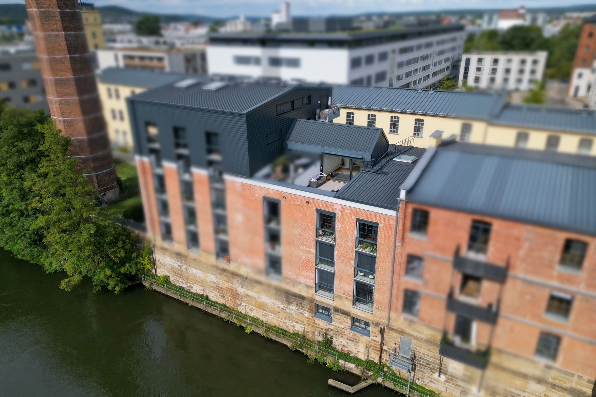 Backsteingebäude mit modernen Fenstern und Dachterrasse direkt am Wasser.