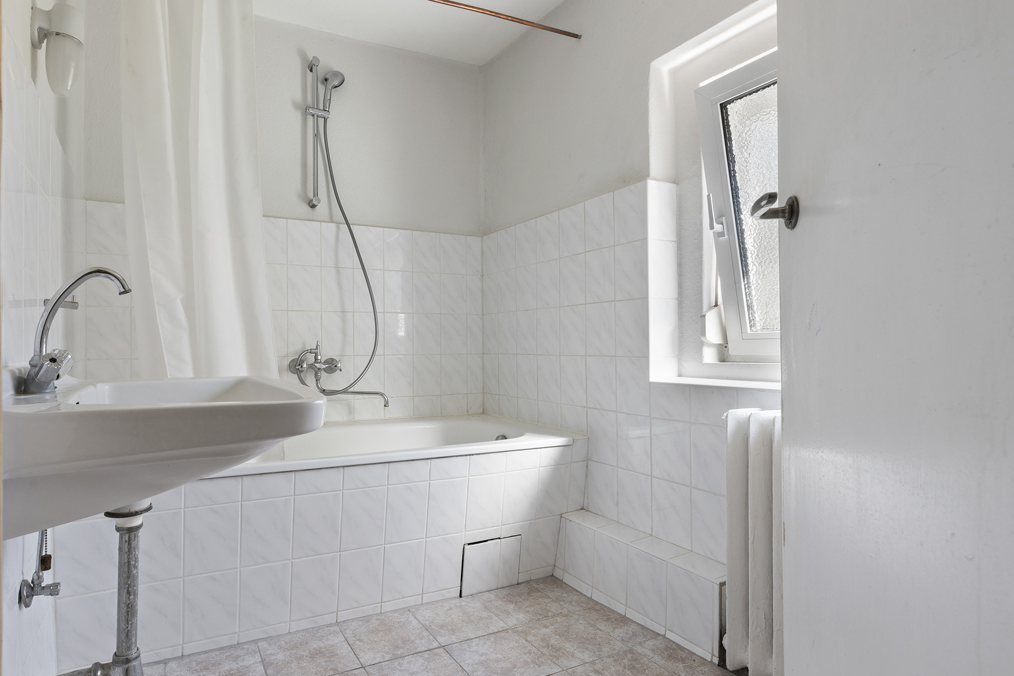 Helles Badezimmer mit Badewanne, Duschvorhang, Waschbecken und geöffnetem Fenster.