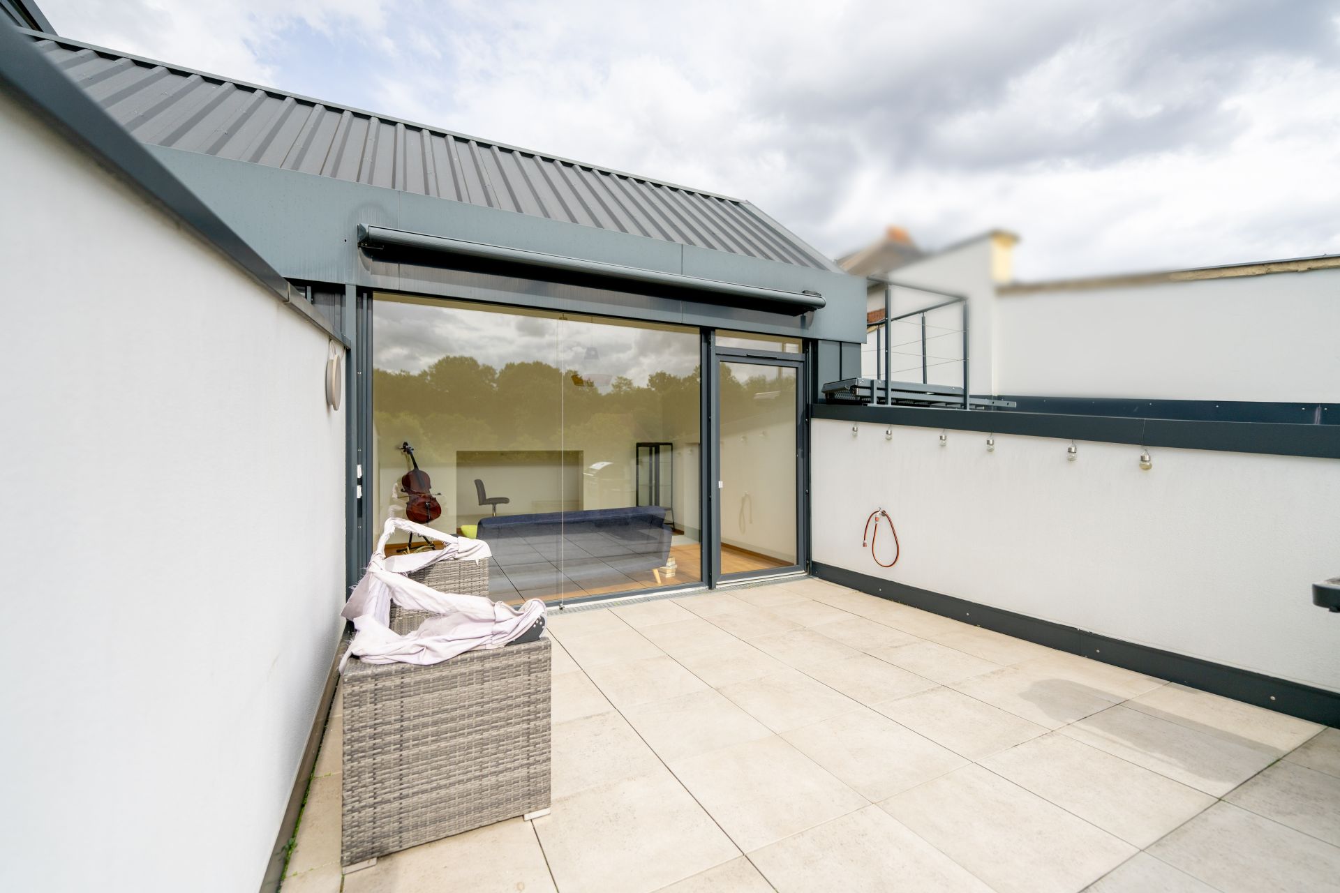 Große Terrasse mit Fliesenboden und Glas-Schiebetür, ein Sitzwürfel vorne links.