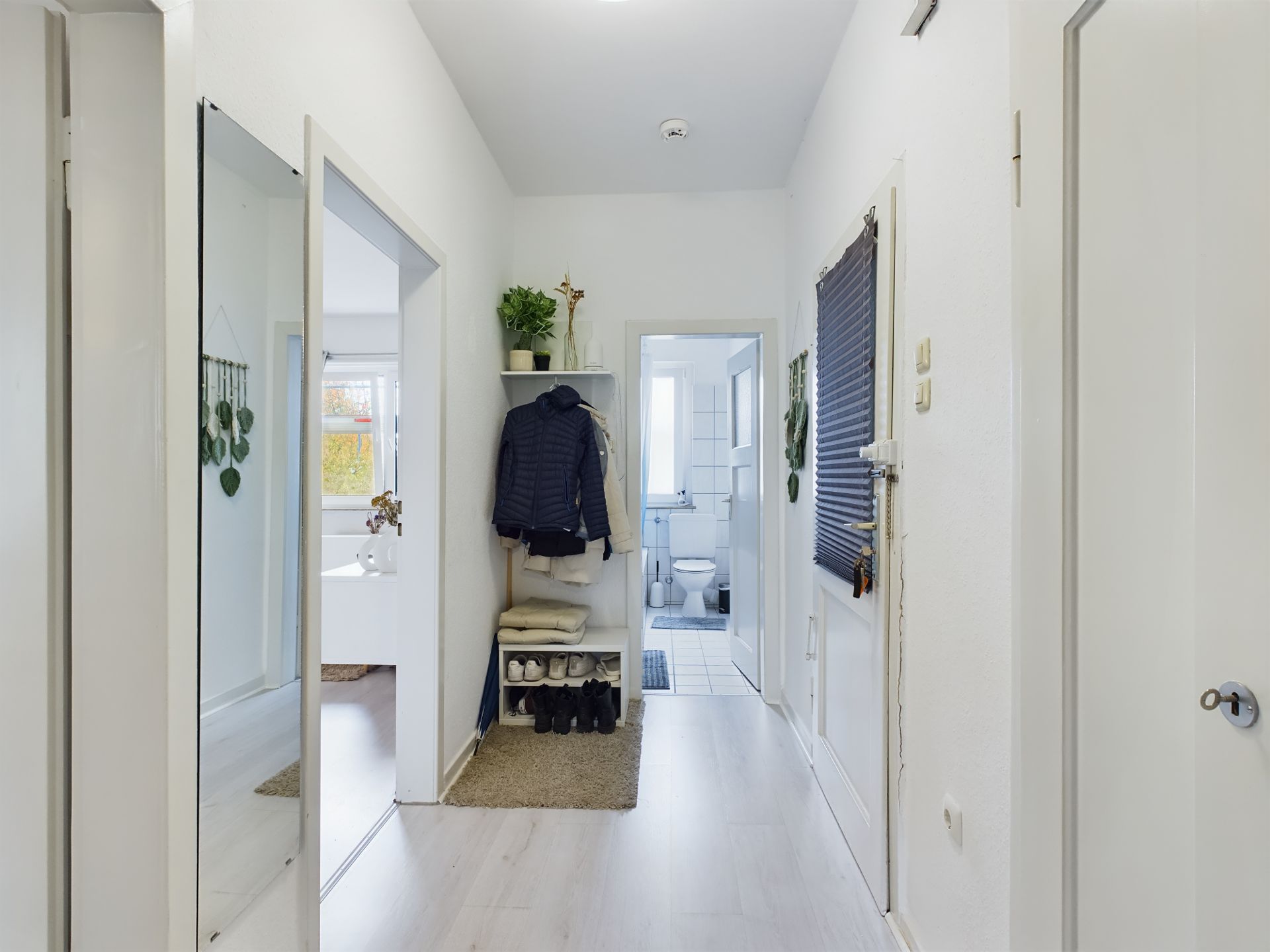 Heller Flur mit Garderobe, Schuhregal, Pflanzen und Blick auf ein Badezimmer.