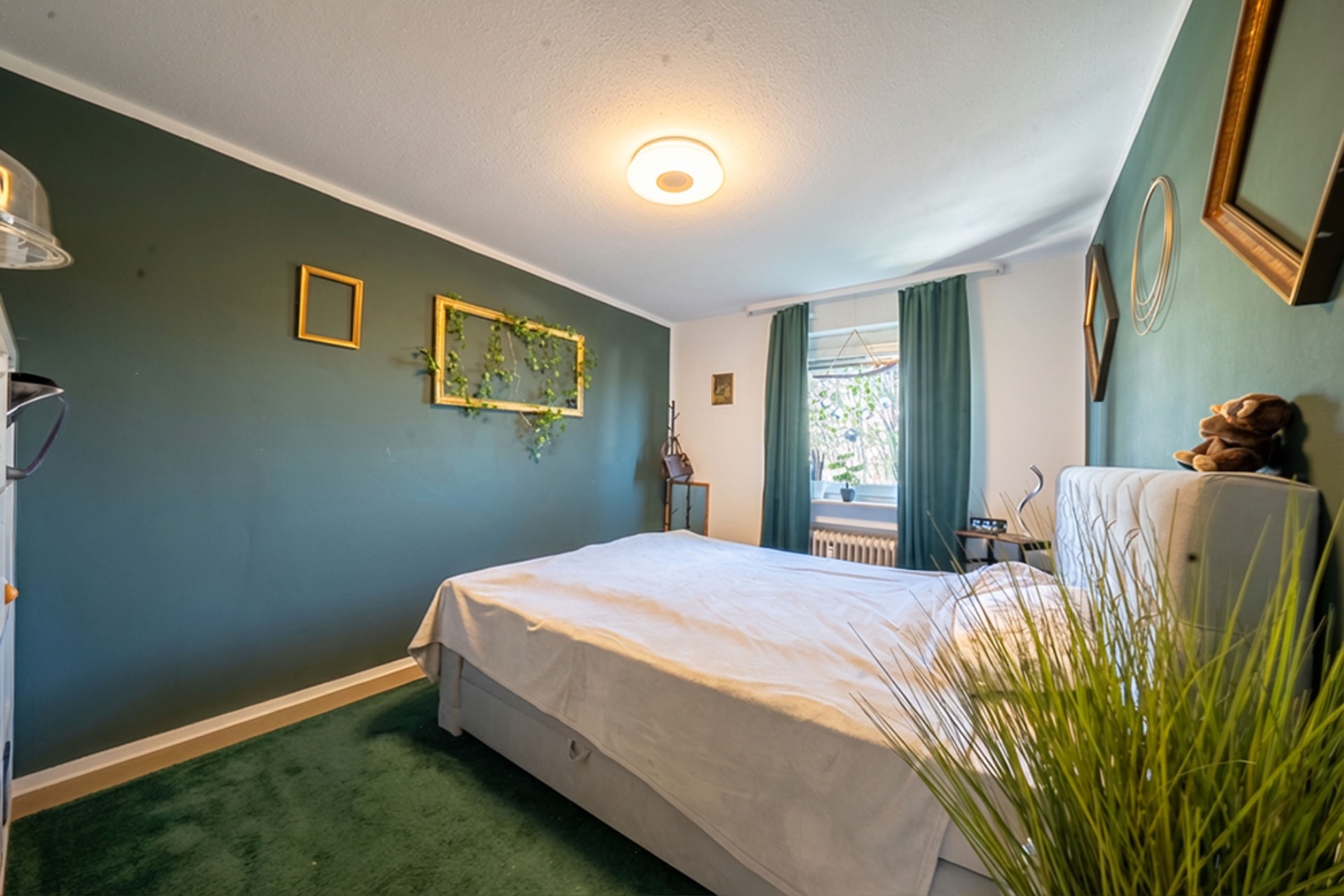 Helles Schlafzimmer mit grünem Teppich, Doppelbett und Dekoration an den Wänden.
