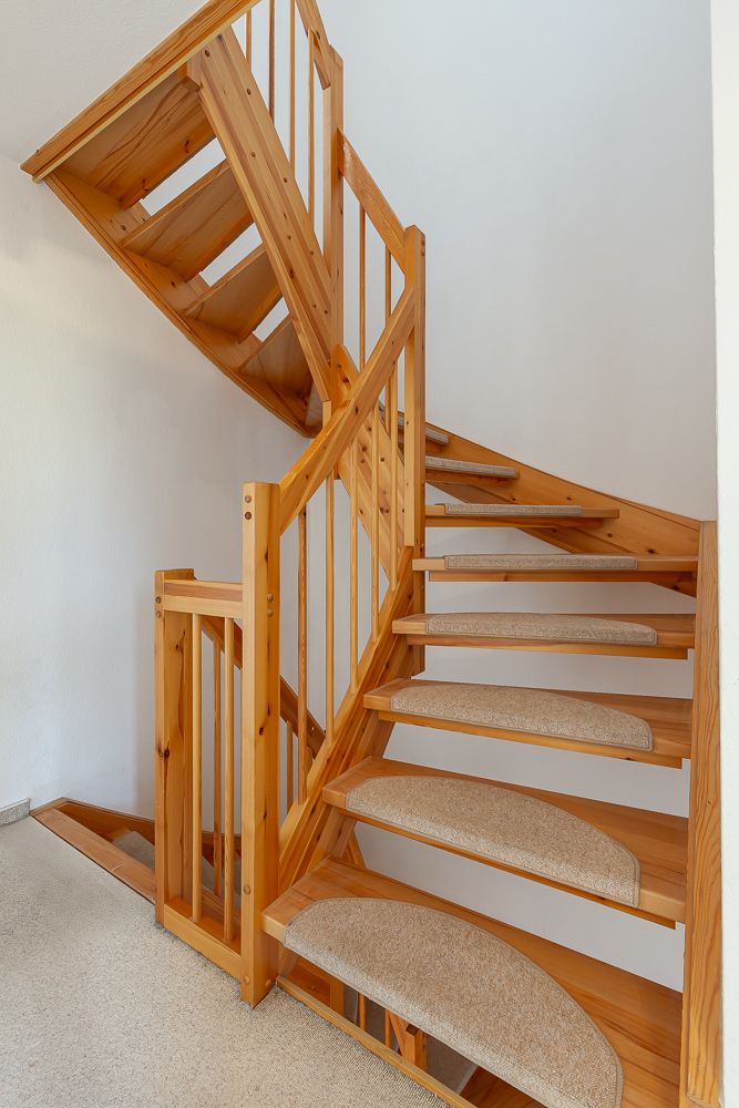 Holztreppe mit Teppichstufen in einem Wohnhaus, helle Wand im Hintergrund.
